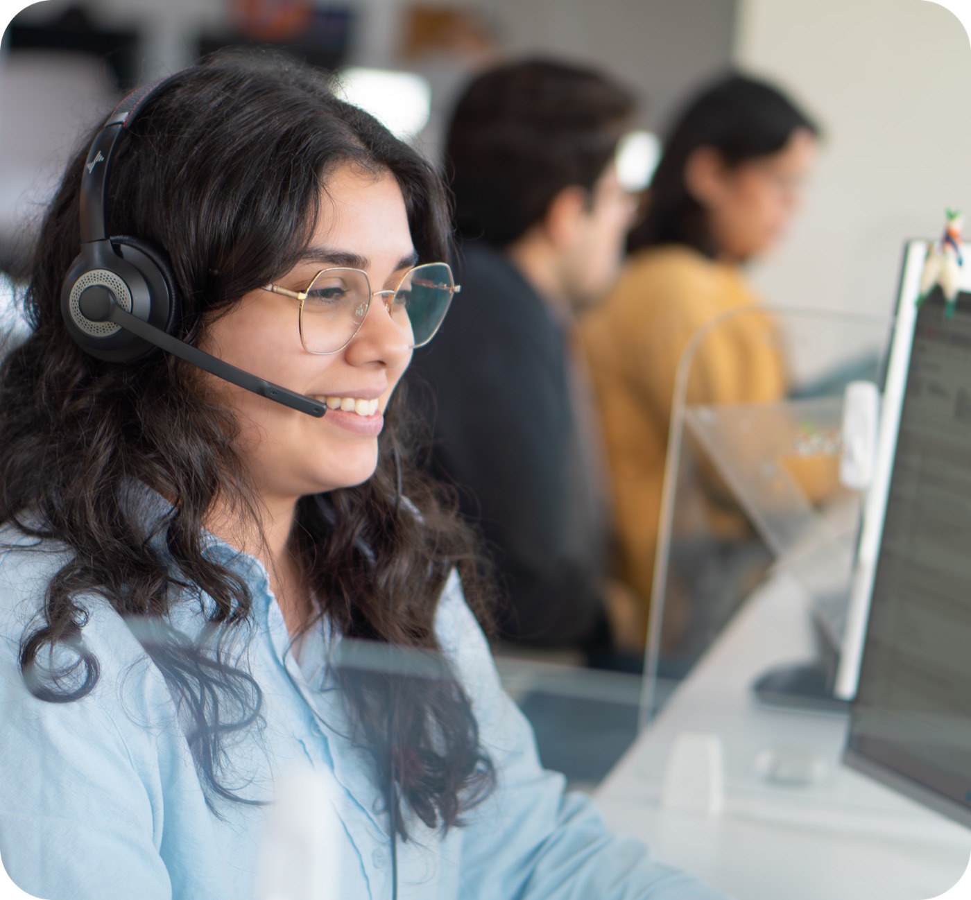 A Work Ninjas call agent, headset on, smiling at her screen with the team bullpen behind her